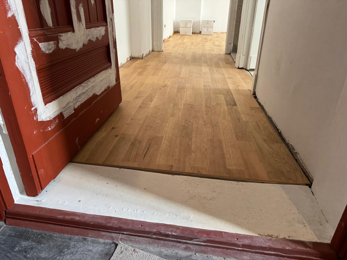 Freshly installed oak strip parquet in a period building hallway with old red door being restored
